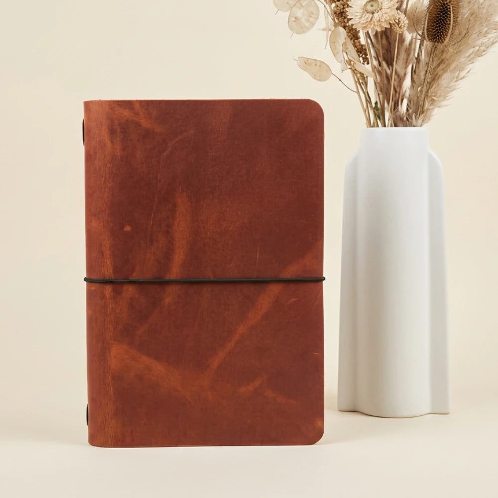 Handmade leather wrap securing a simple writing journal with flexible elastic support.