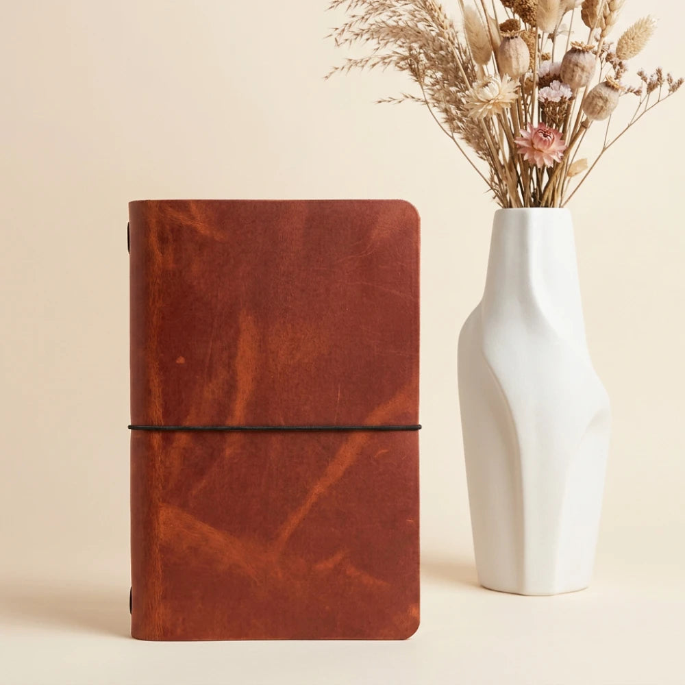 Handcrafted leather journal cover holding a simple notebook securely inside with elastic.