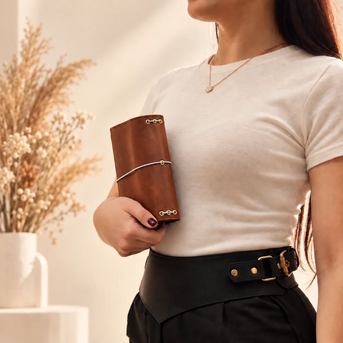 Woman showcasing a natural leather notebook cover while gently holding it with both hands.