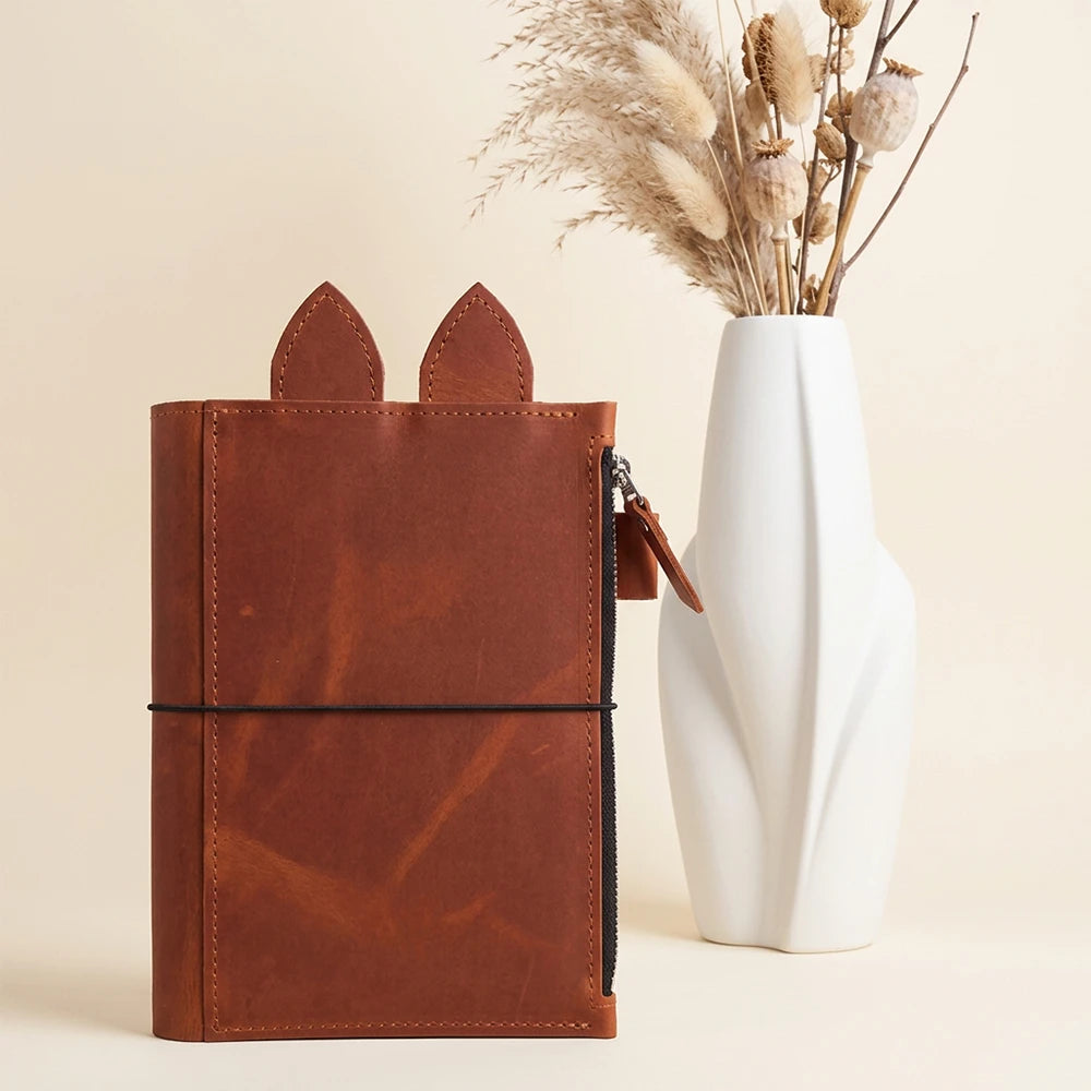 Handmade leather journal cover featuring zipper pocket, pen holder, decorative leather ears, and three elastics.