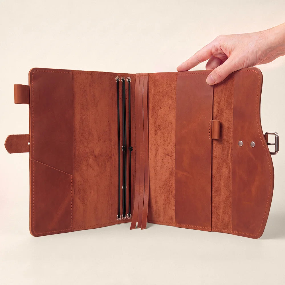 Natural leather notebook holder with inner pockets, pen loop, bookmark ribbon, and sturdy carrying grip.