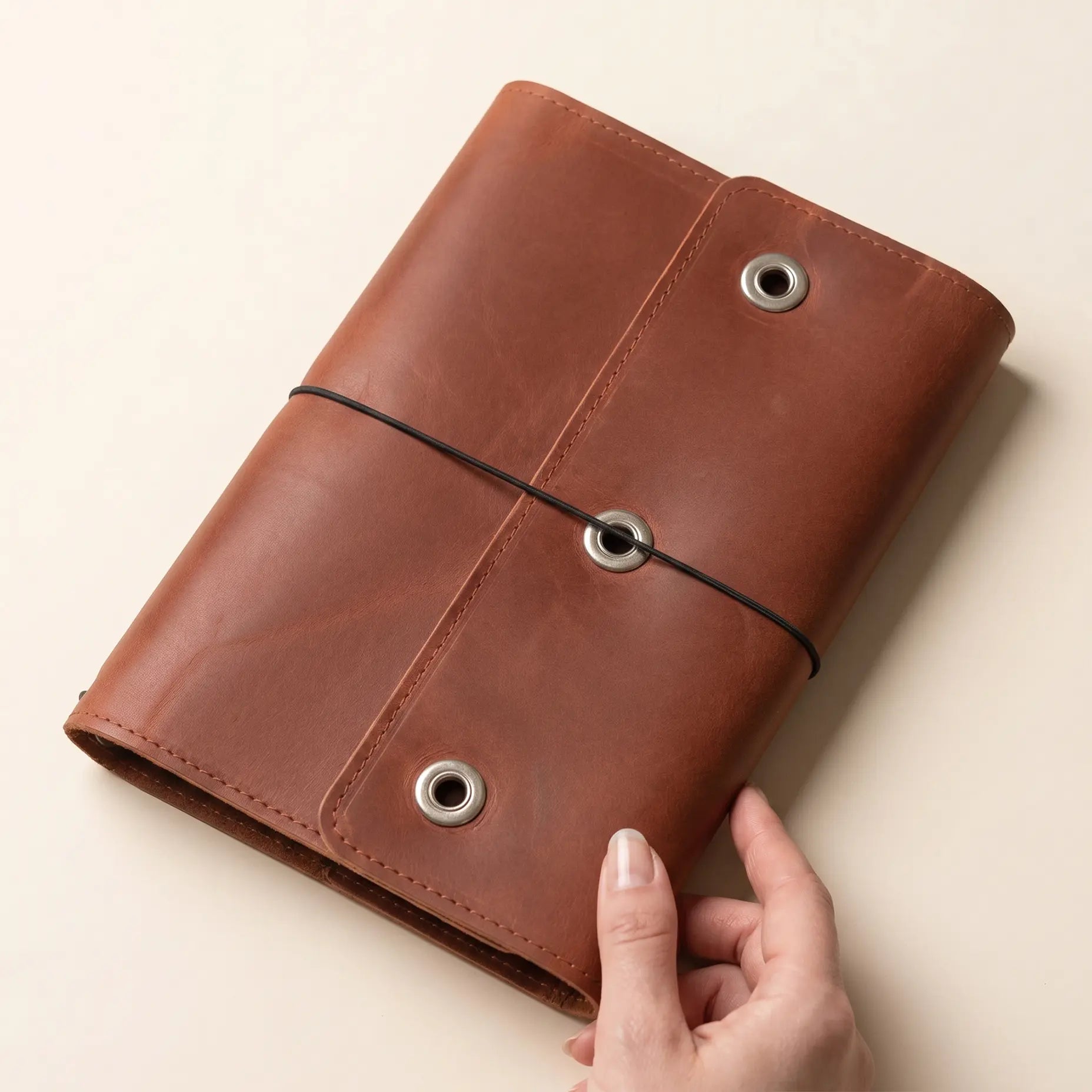 Leather travel journal cover with three elastics and storage pockets.