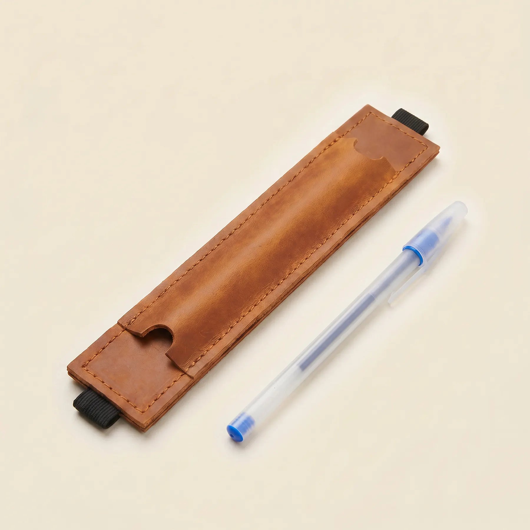 Genuine leather pen holder with elastic band securely attached to a hardcover notebook.