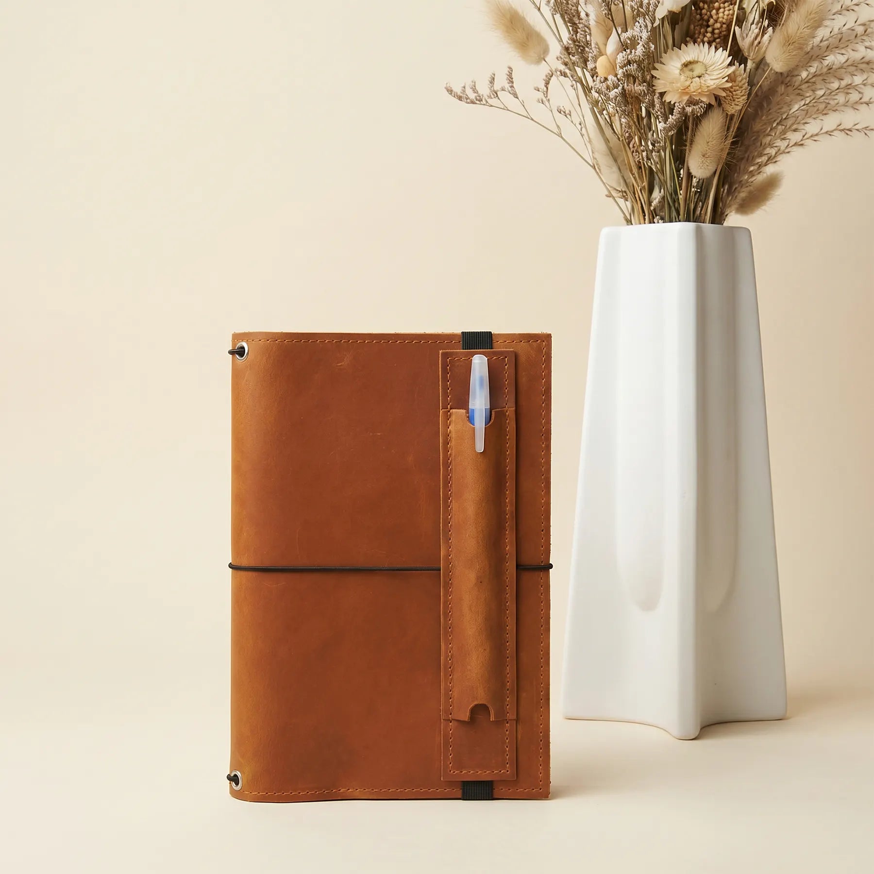 Minimalist leather pen holder attached to notebook using durable elastic band design.