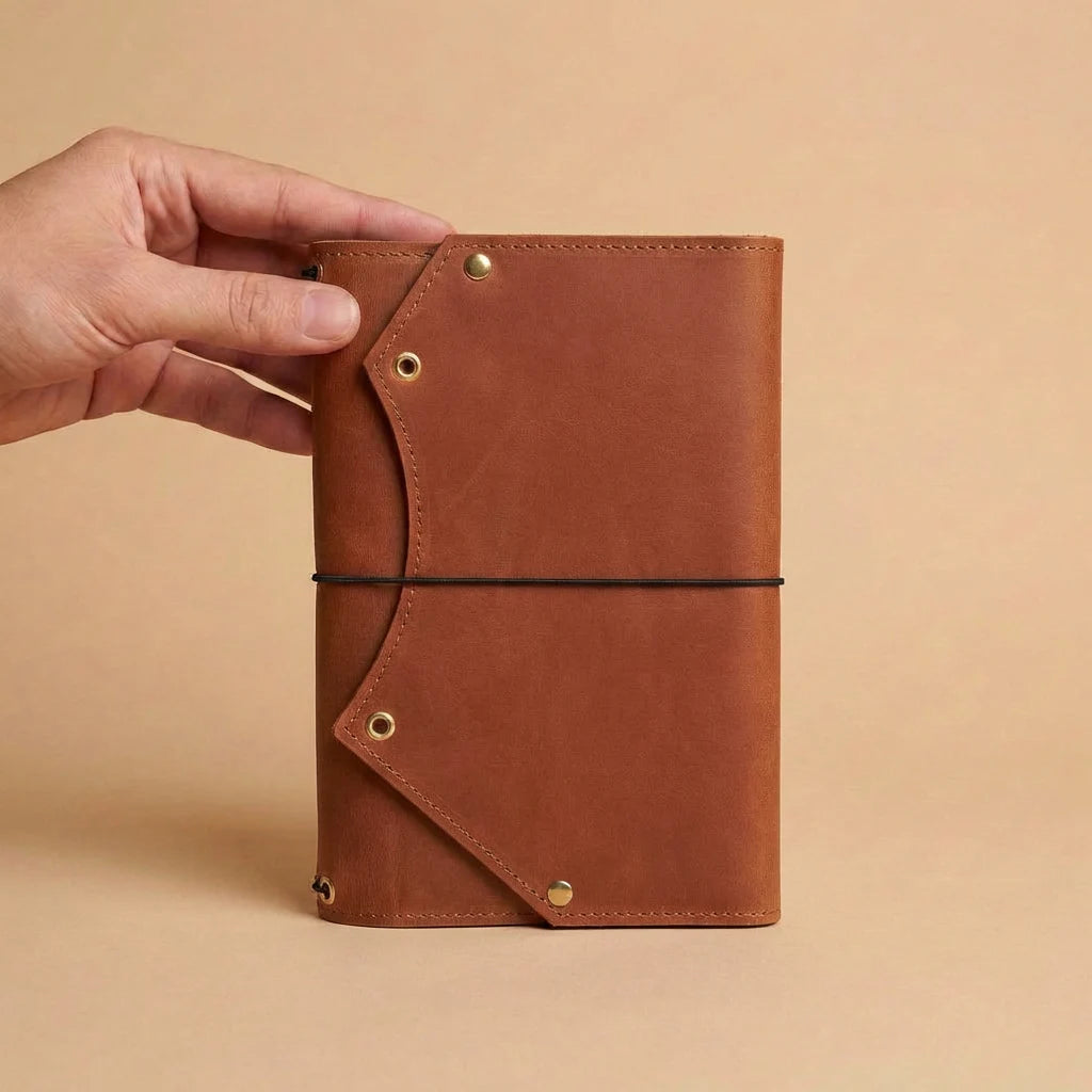 Brown leather notebook held by a hand against a beige background