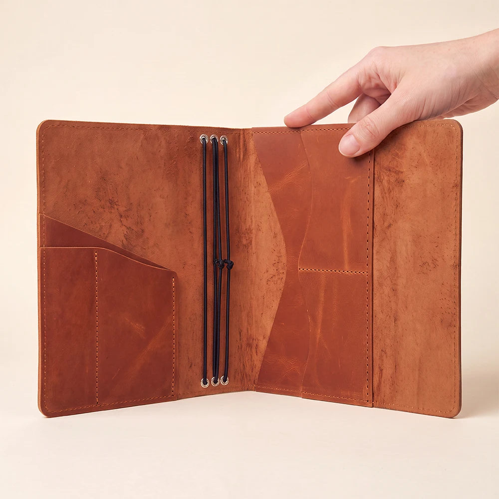 Refillable leather notebook cover with inner pockets, pen loop, and three elastic holders.
