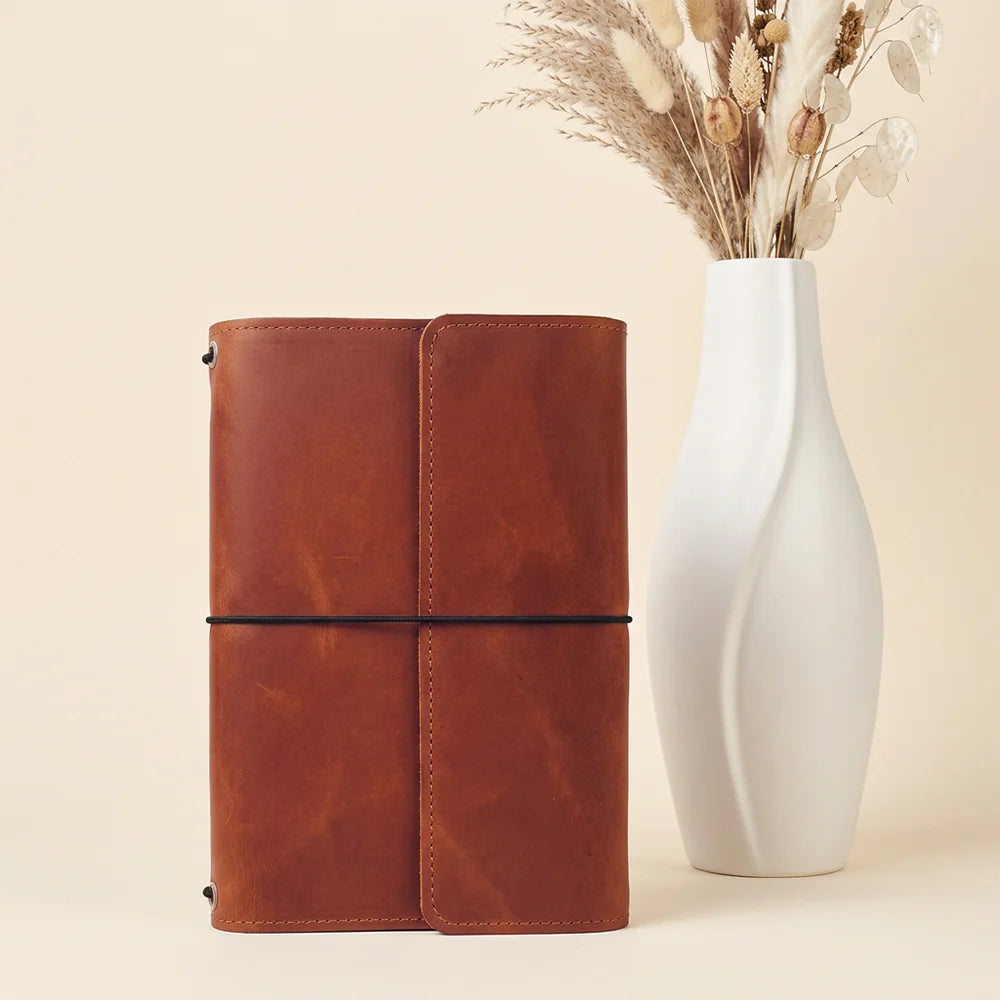 Natural leather planner sleeve with interior storage pockets and convenient writing instrument accommodation.
