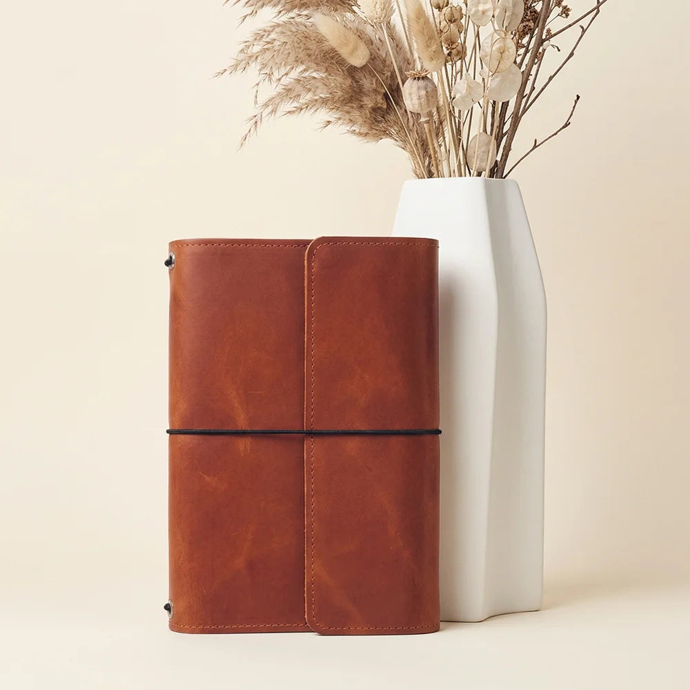 Genuine leather journal organizer with detailed stitching, interior compartments, and convenient writing tool storage.