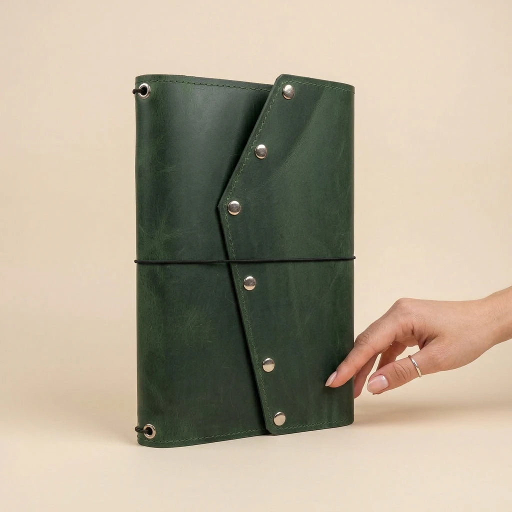 Green leather journal with silver buttons held by a hand on a beige background