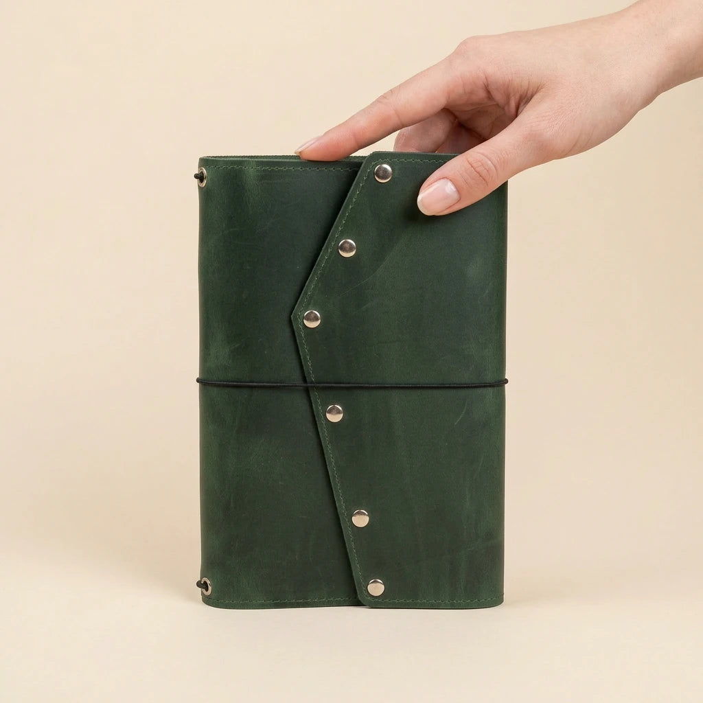 Green leather notebook held by a hand on a beige background