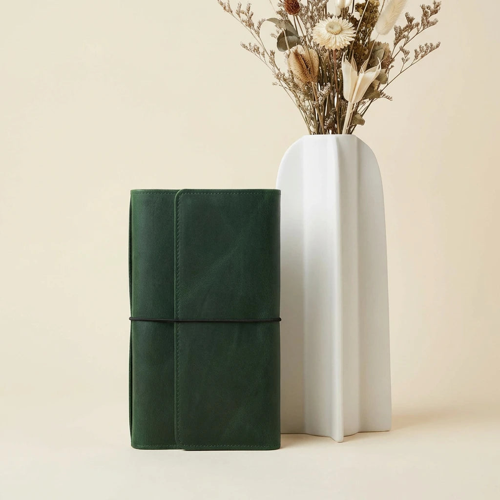 Green leather-bound book and white ceramic vase with dried flowers on a beige background