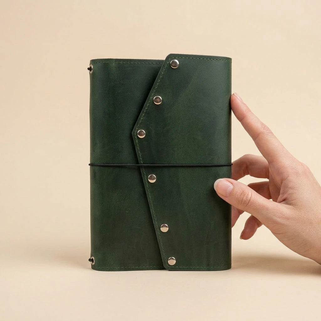 Green leather notebook held by a hand against a beige background