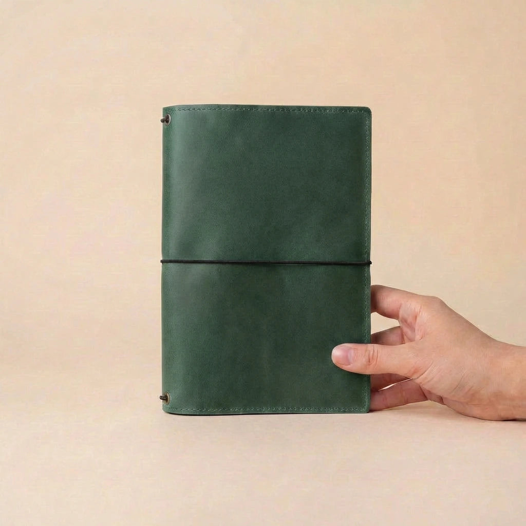 Green leather notebook held by a hand against a beige background