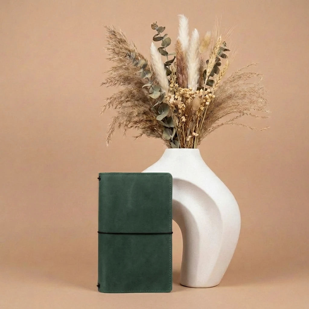 Green notebook next to a white vase with dried plants on a beige background