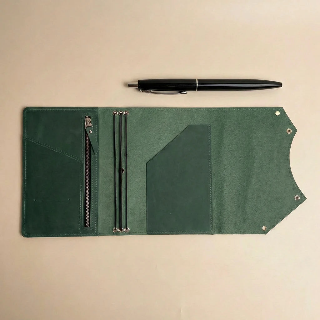 Green leather journal cover with pen holder and pen on a beige background