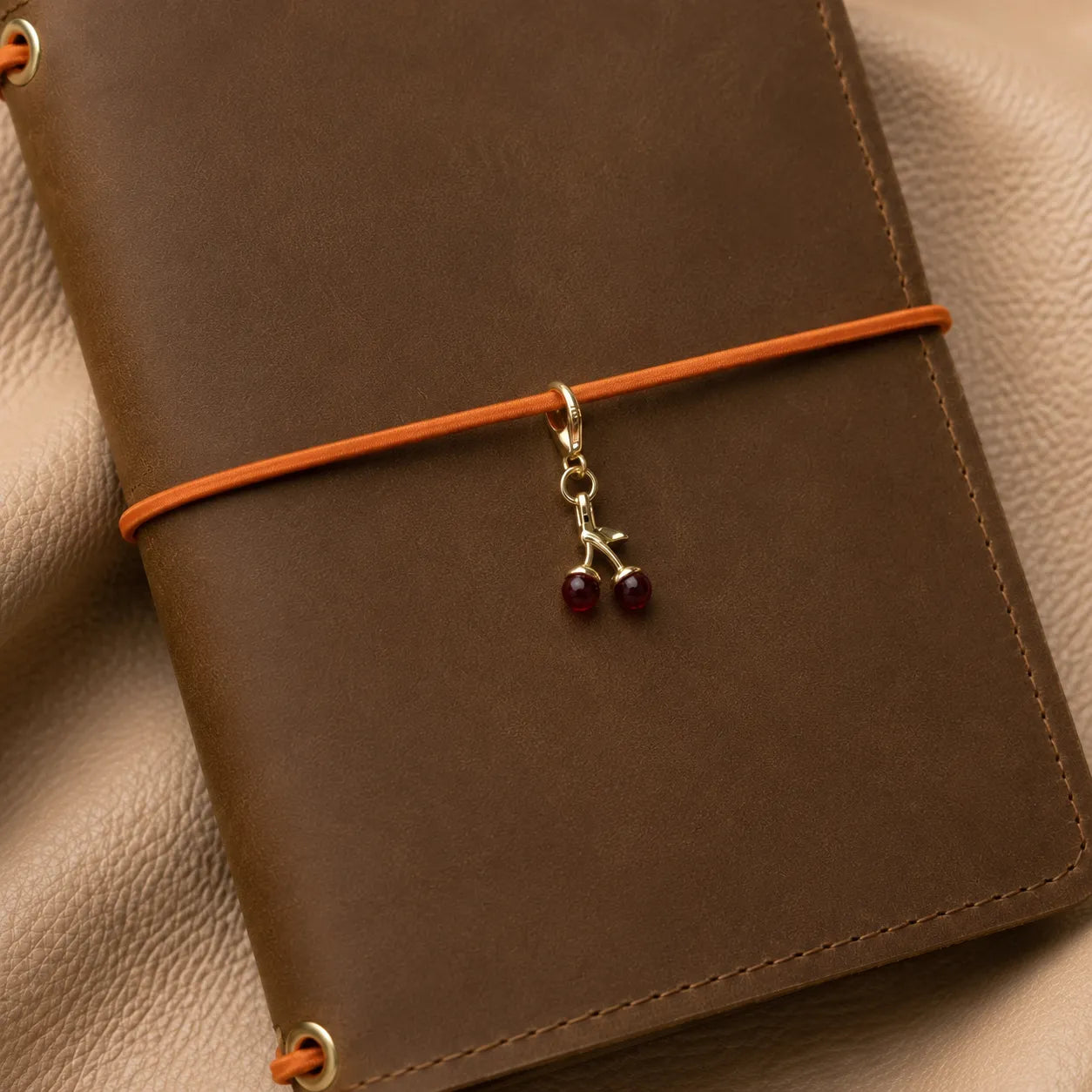 Cute cherry notebook charm hanging from elastic bands, stylish journal accessory with metal hardware.