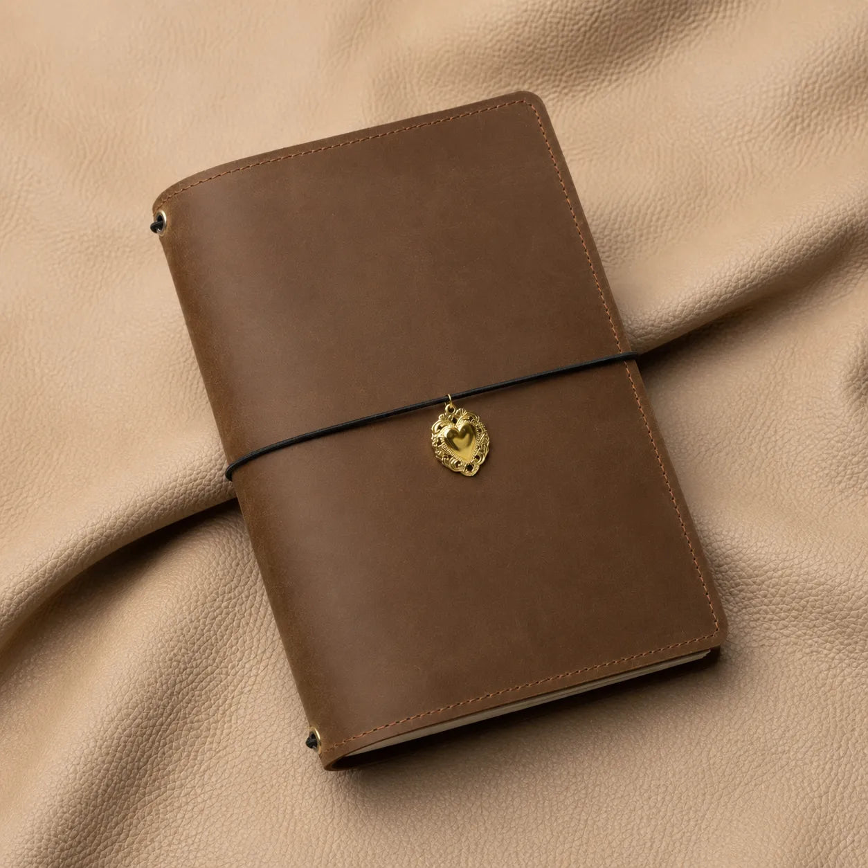 Minimalist heart notebook charm accessory attached to elastic band inside leather journal cover.