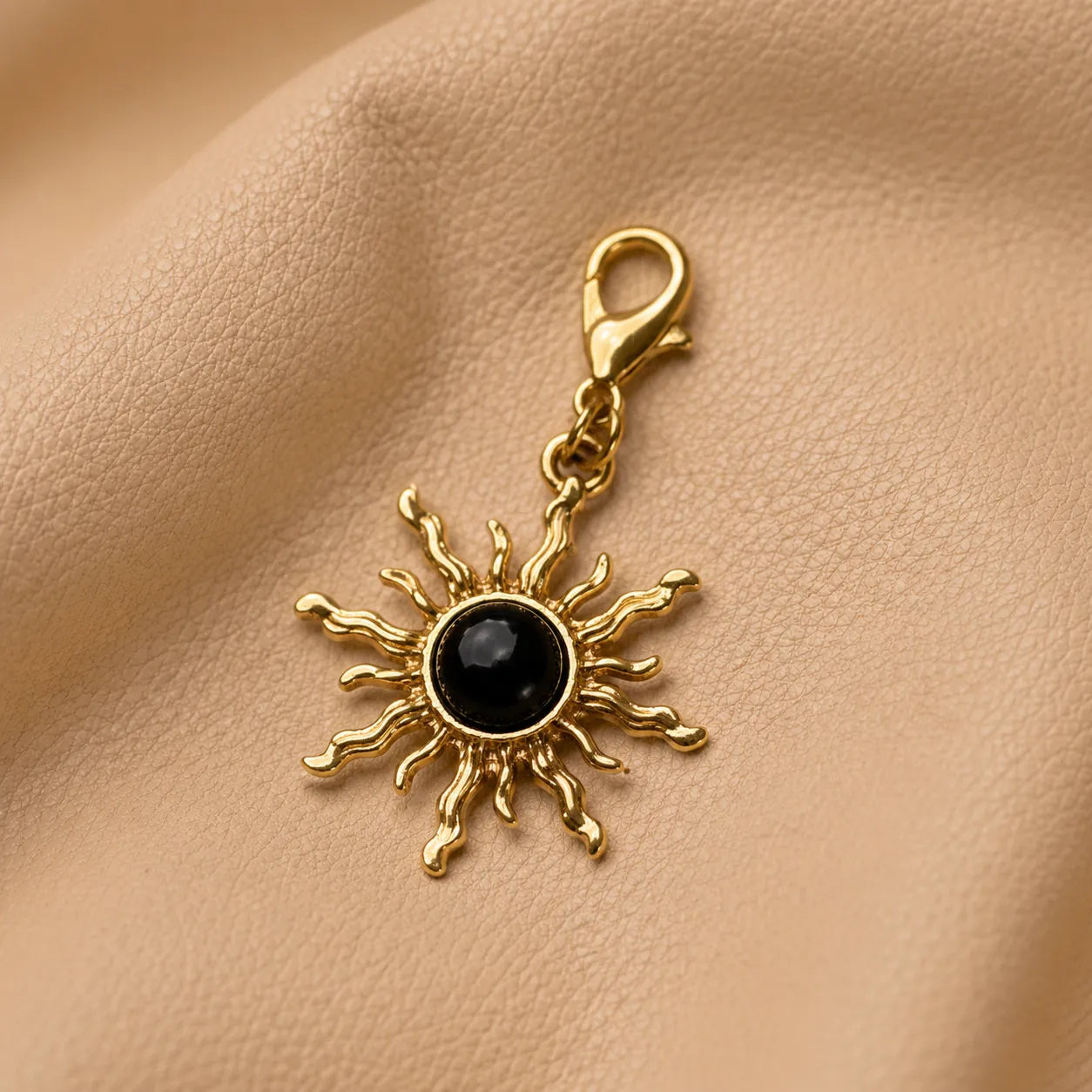 Sun-shaped journal charm with black center stone attached to a leather notebook elastic.