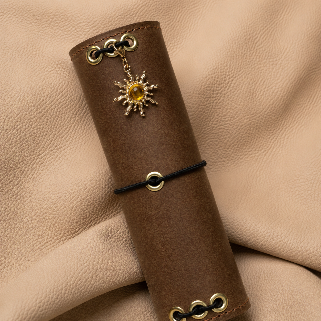 Close-up of a sun-shaped journal charm with black center detail on a leather notebook cover.