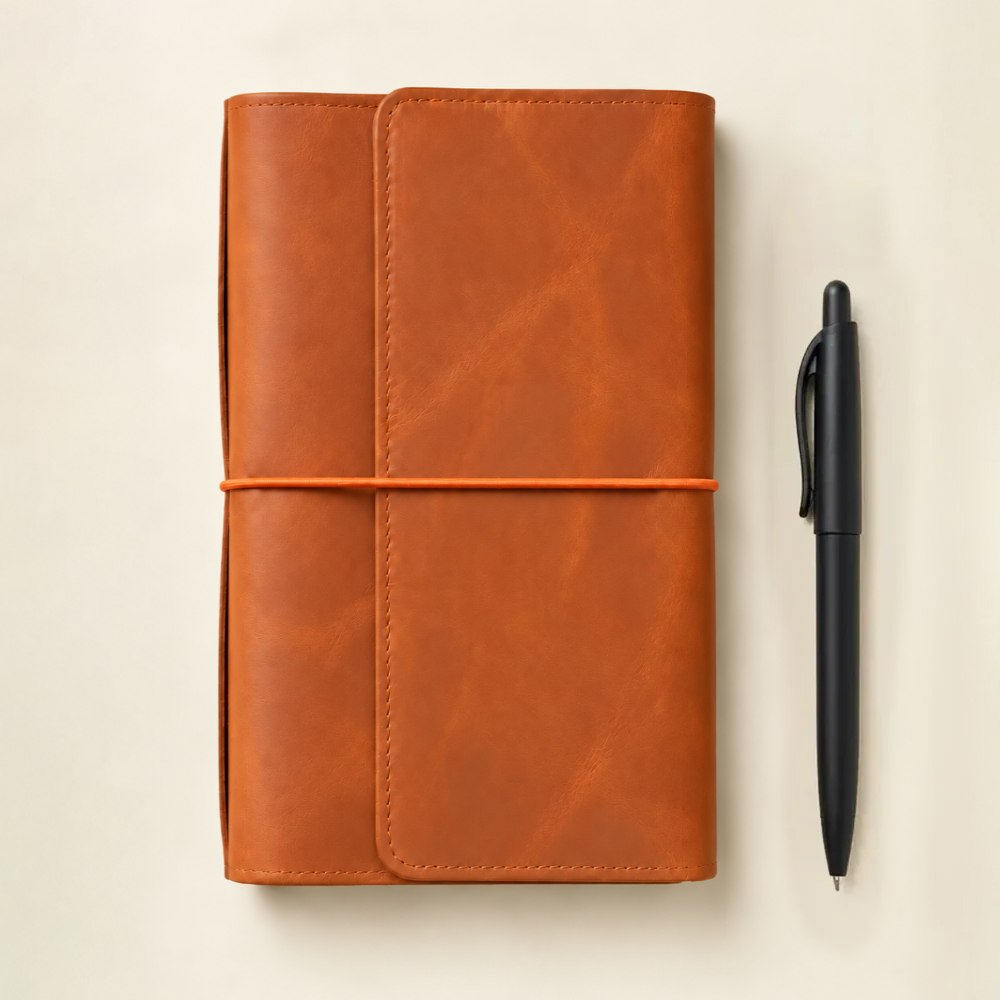 Handmade leather notebook cover in orange with six elastic bands and organized interior pockets.