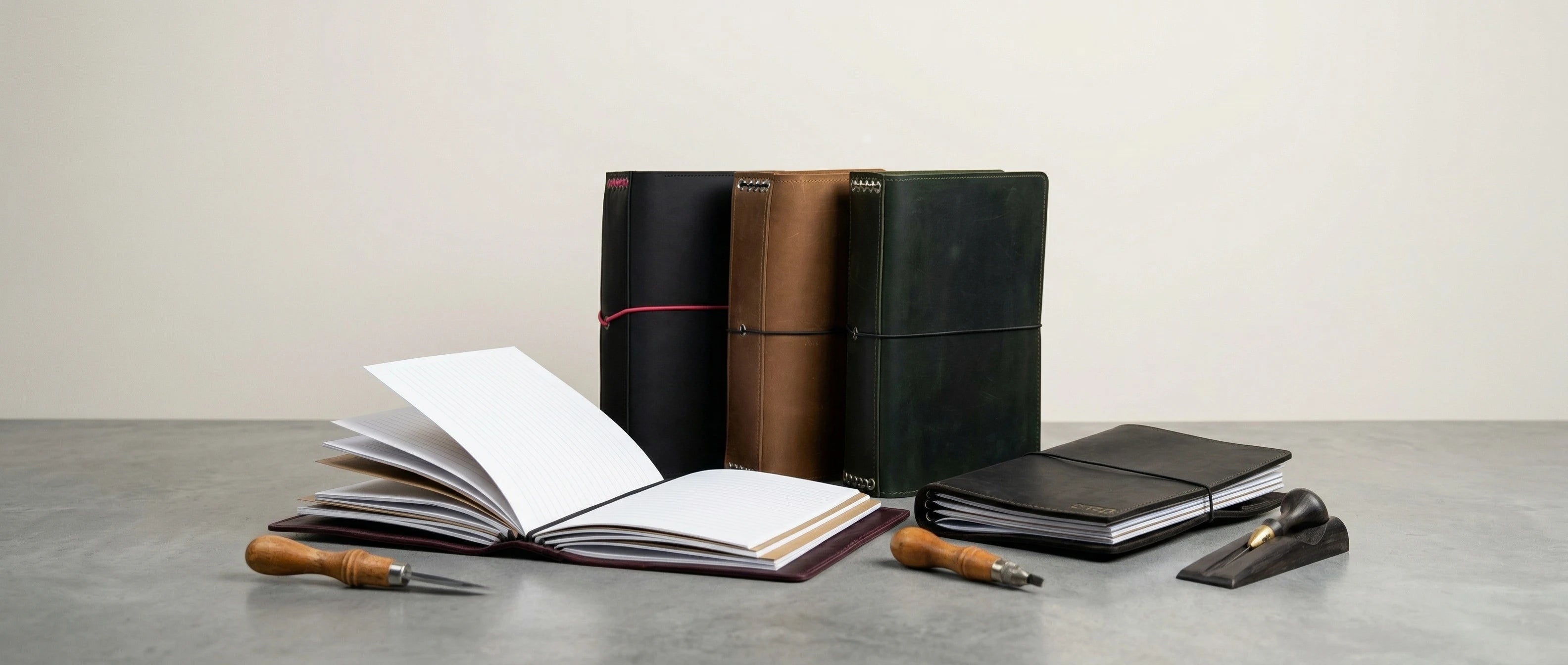 Set of leather-bound notebooks and writing instruments on a gray surface with a light background