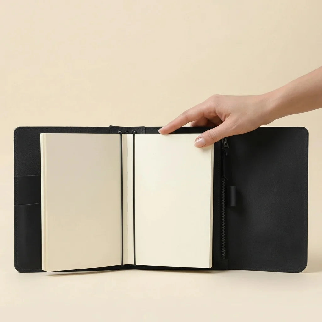 Black leather-bound notebook with a hand opening it on a beige background