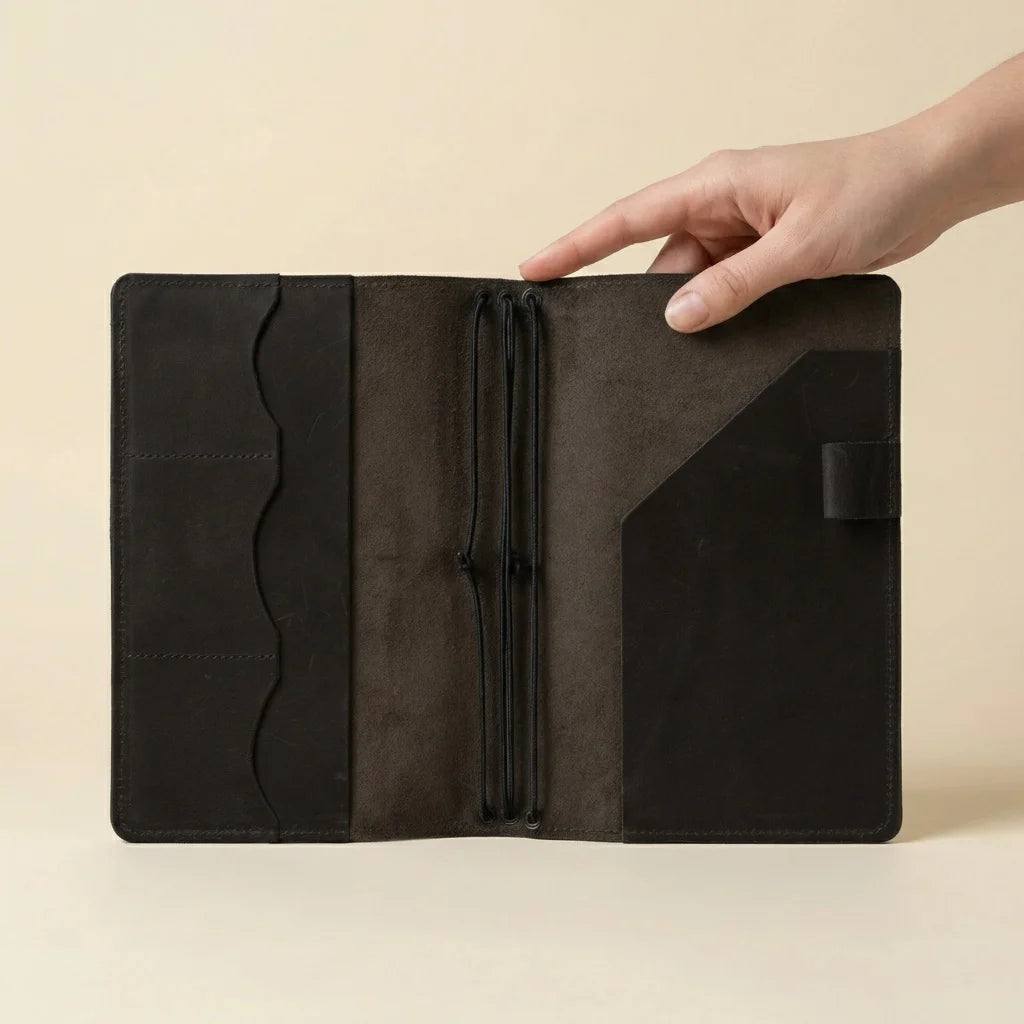 Hand holding a black leather journal against a beige background