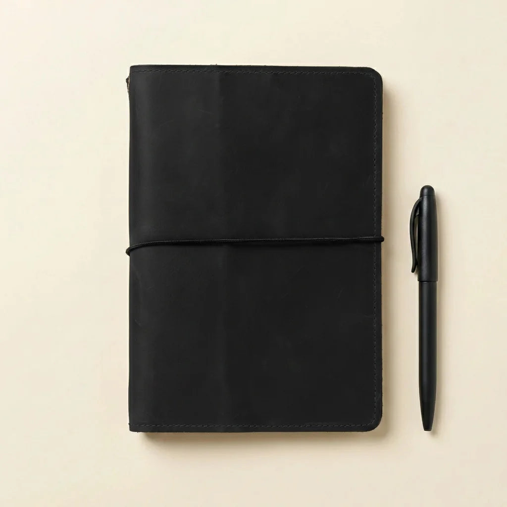 Black leather notebook next to a white vase with dried flowers on a beige background
