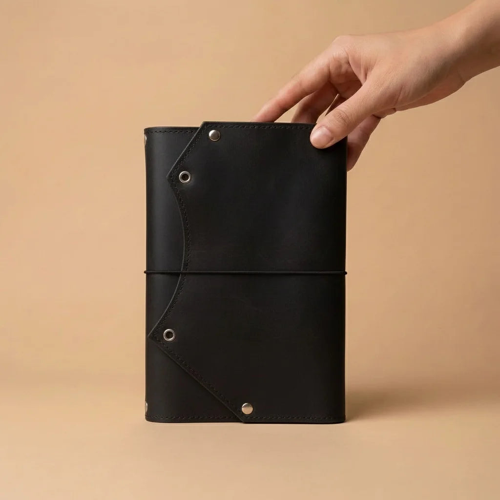 Black leather notebook held by a hand against a beige background