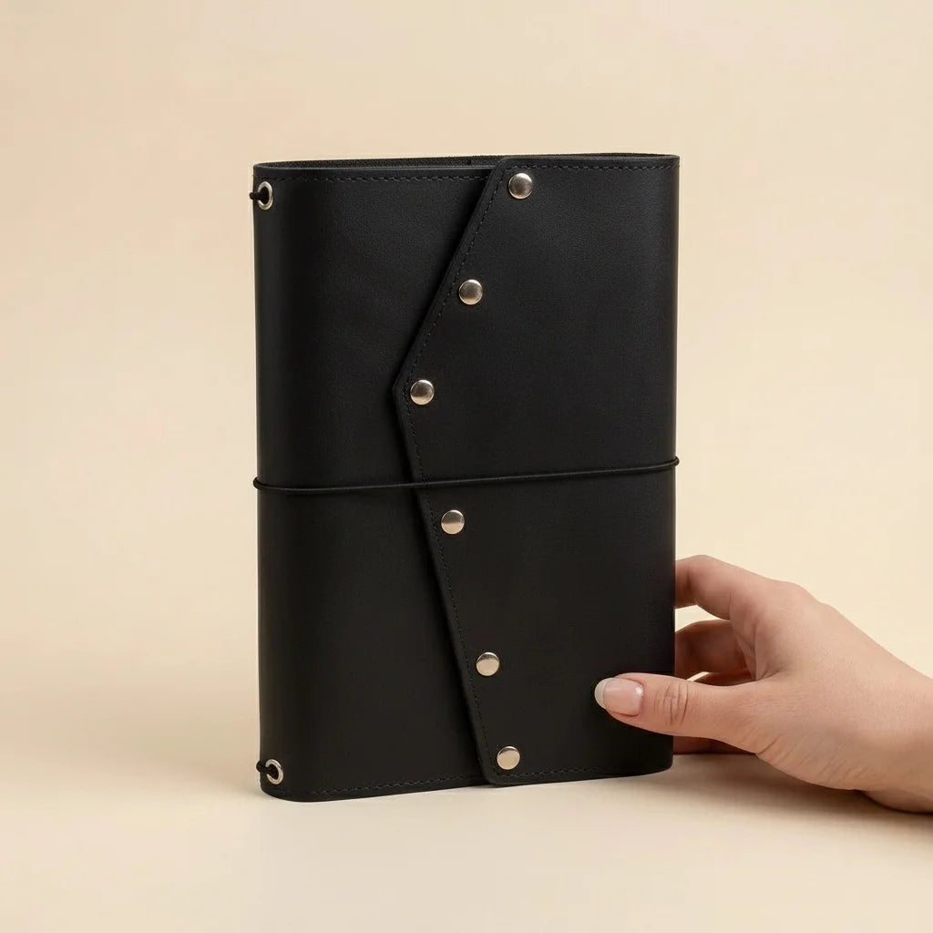 Black leather notebook held by a hand on a beige background