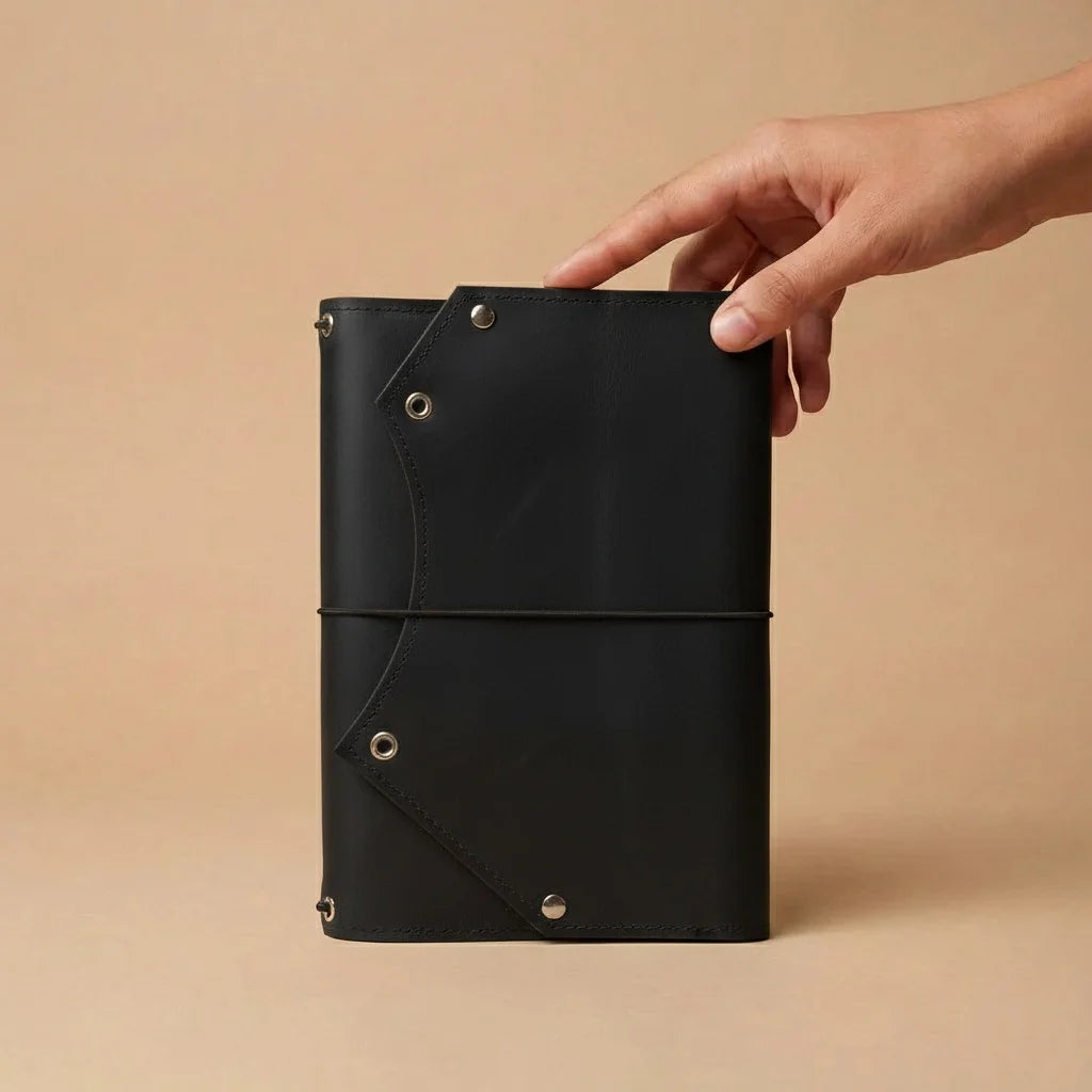 Black leather notebook held by a hand against a beige background