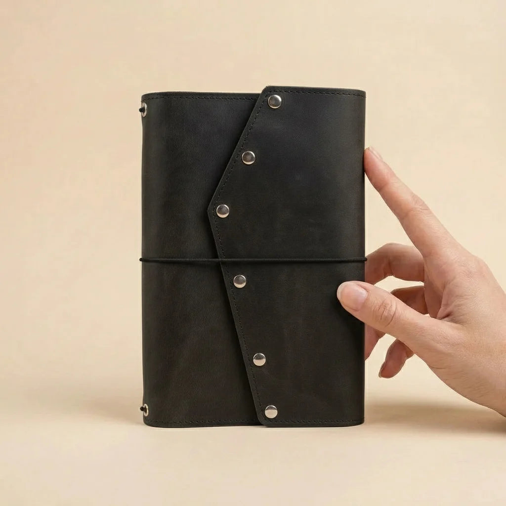 Black leather notebook held by a hand on a beige background