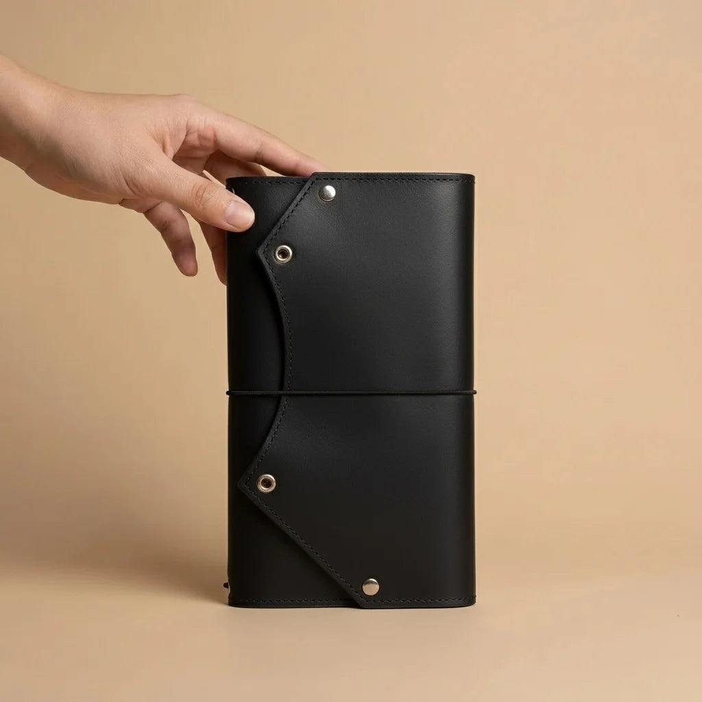 Black leather notebook held by a hand against a beige background
