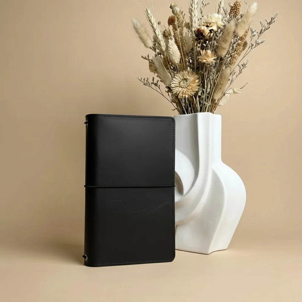 Black leather wallet next to a white vase with dried flowers on a beige background