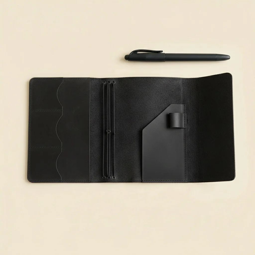 Black leather notebook with pen holder on a beige background