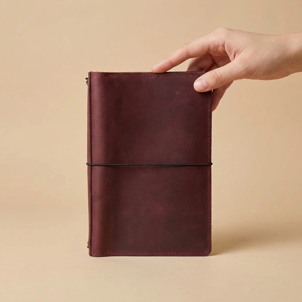 Hand holding a maroon leather notebook against a beige background
