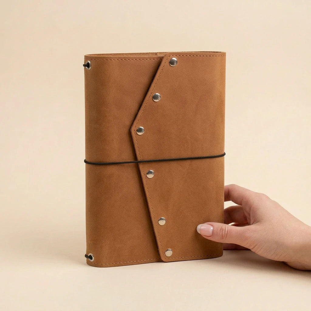 Brown leather notebook held by a hand on a beige background