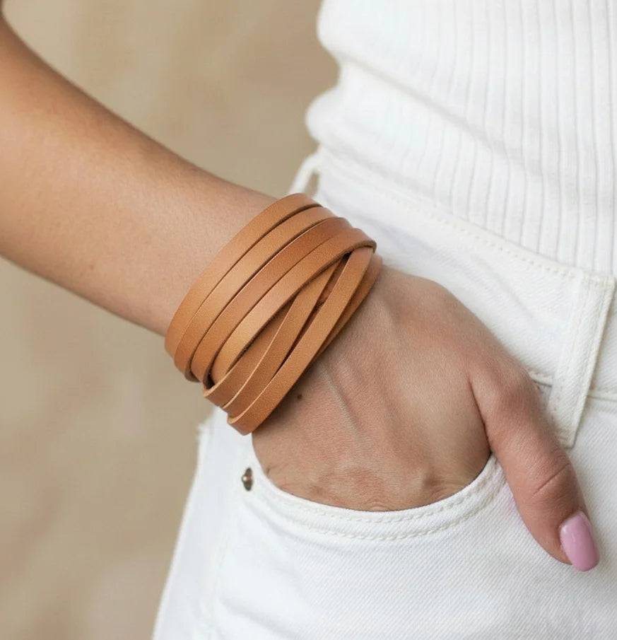 Person wearing a brown leather bracelet on a neutral background
